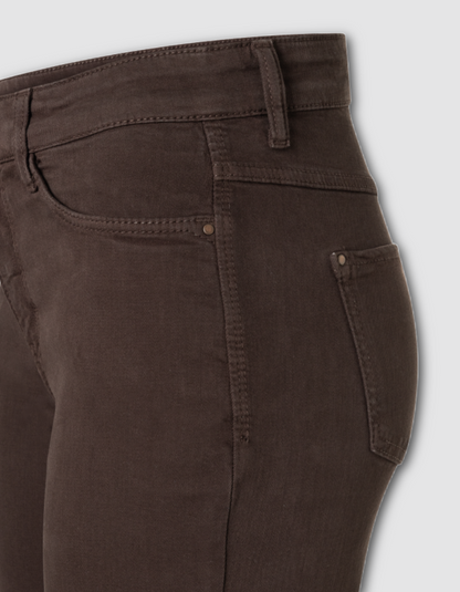 Close-up of the back waistband and right rear pocket of dark brown denim jeans, showing stitching and a buttoned pocket on a light gray background.