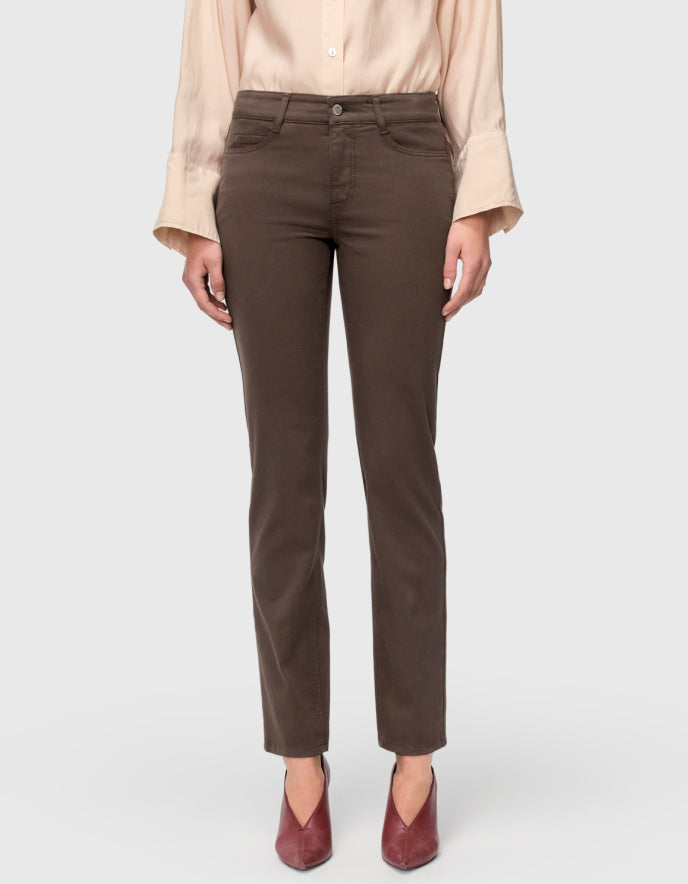 A model from the waist down wearing dark brown straight-leg jeans, a light beige blouse, and burgundy pointed-toe heels, set against a plain light gray studio background.