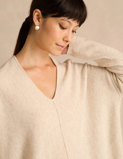 A woman wearing a soft cream-colored V-neck knit sweater, shown in a close-up portrait against a warm beige background.