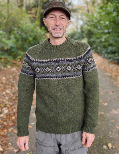 Man wearing a green knitted sweater with a patterned design outdoors.