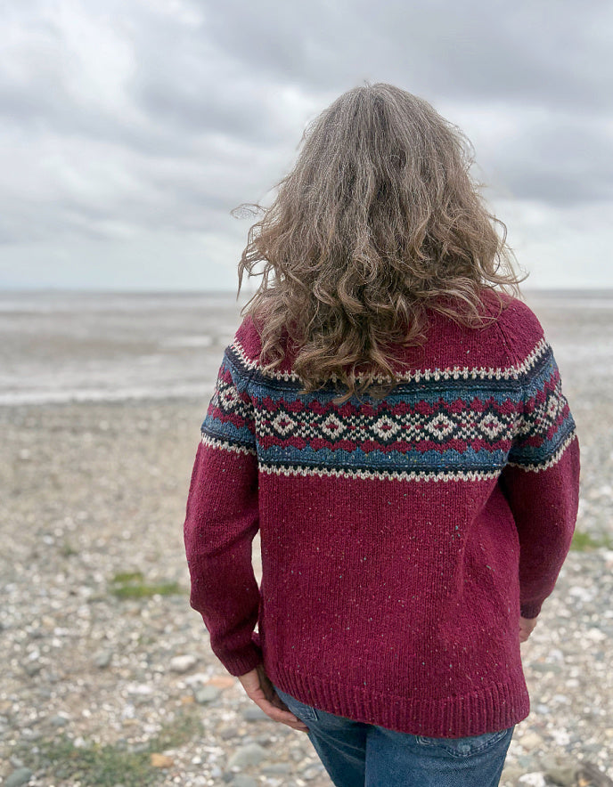 Person wearing a red Fair Isle patterned sweater standing in a grassy field