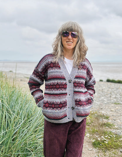Woman wearing a fair Isle cardigan and plum cord trousers and sunglasses standing by a beach.