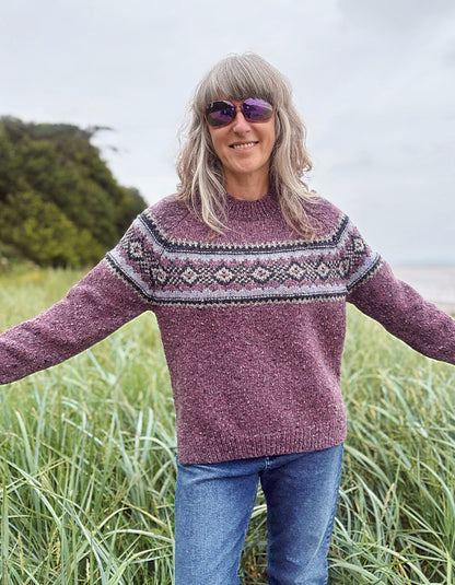 Person wearing a patterned berry Fair Isle sweater and sunglasses in a field