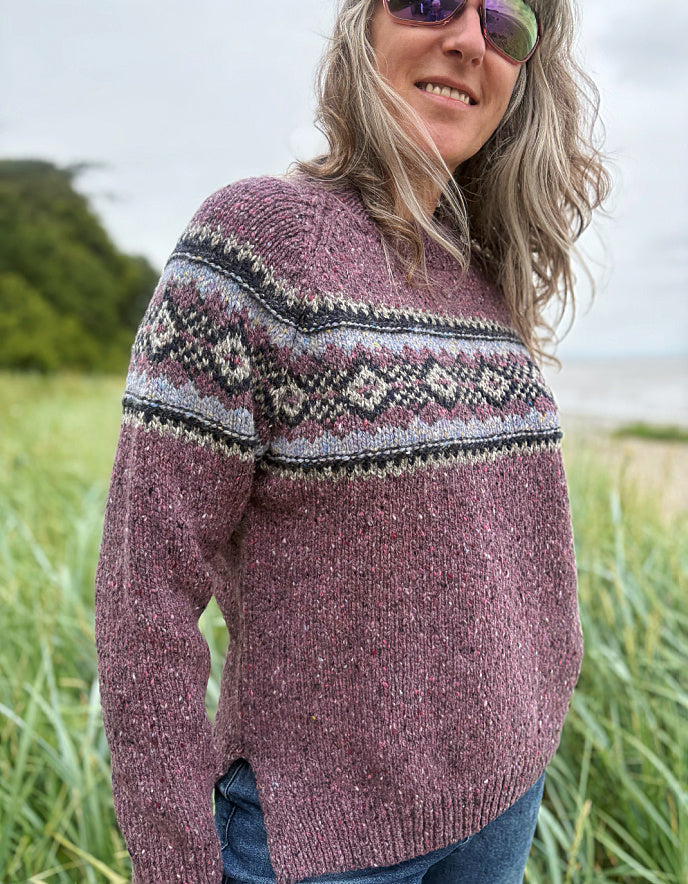Person wearing a patterned berry Fair Isle sweater and sunglasses in a field