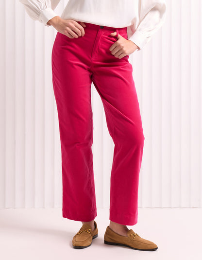 Woman wearing a white blouse and bright pink velvet pants against a white background