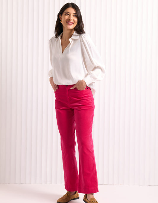 Woman wearing a white blouse and bright pink velvet pants against a white background