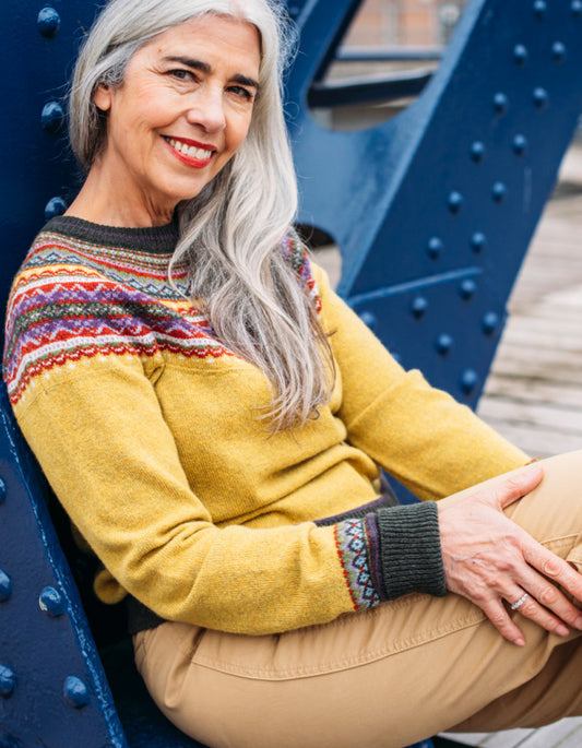 Woman wearing a ochre yellow Fair isle sweater sitting on a blue metal structure.