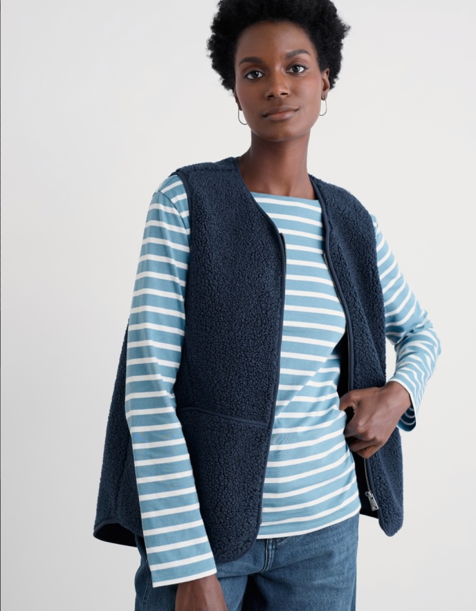 Woman wearing a blue striped shirt and navy vest against a white background