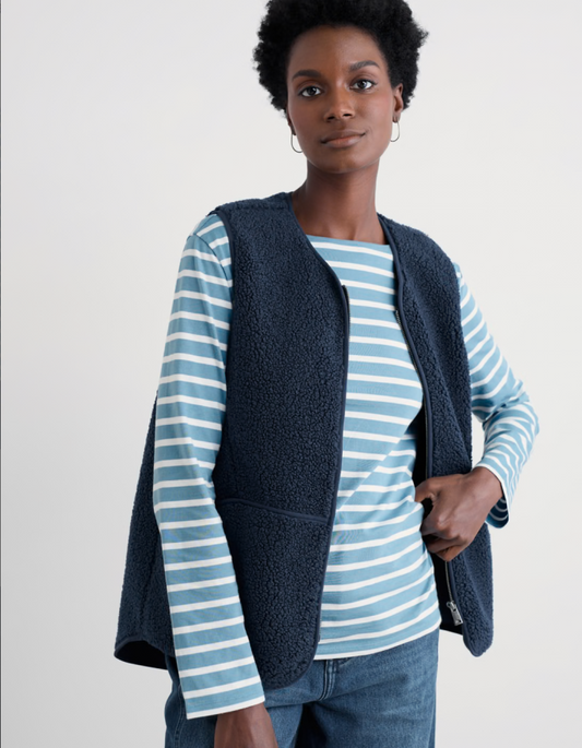 Woman wearing a blue striped shirt and navy vest against a white background