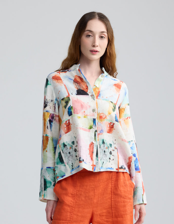 Woman wearing a colorful floral blouse with orange pants on a gray background