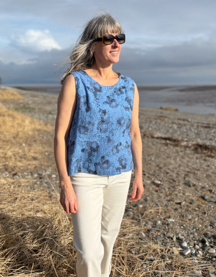 Woman wearing a blue sleeveless top and sunglasses standing in a field with a scenic background.