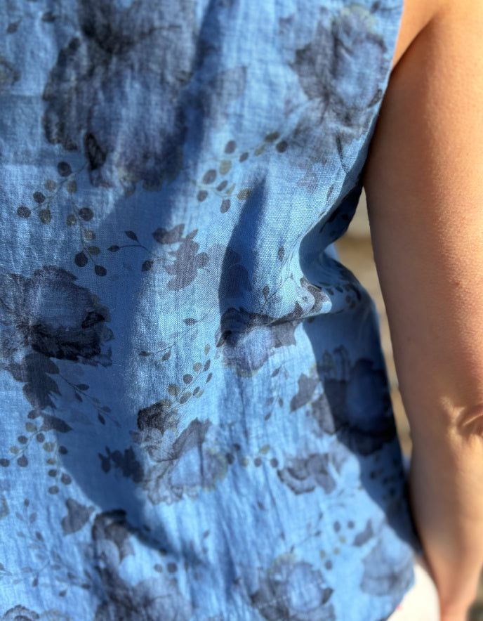 Woman wearing a blue sleeveless top and sunglasses standing in a field with a scenic background.