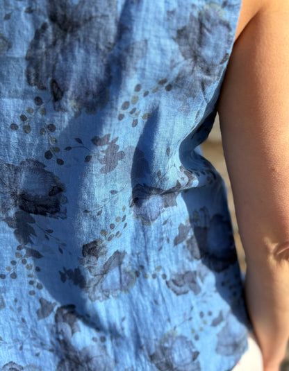 Woman wearing a blue sleeveless top and sunglasses standing in a field with a scenic background.