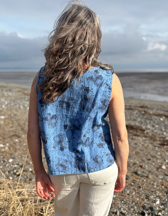 Woman wearing a blue sleeveless top and sunglasses standing in a field with a scenic background.