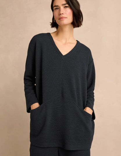 A woman wearing a navy V-neck long-sleeve tunic with side pockets, posed against a solid beige background.