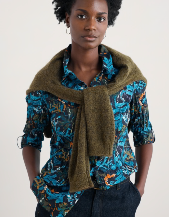 Woman wearing a patterned shirt with a green scarf against a plain background