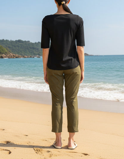 Person standing on a beach wearing a black top and green pants.