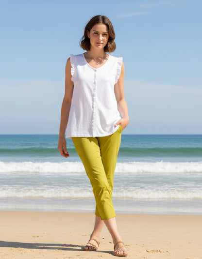 Woman in white sleeveless top and lime trapeze pants standing on a beach with ocean in the background