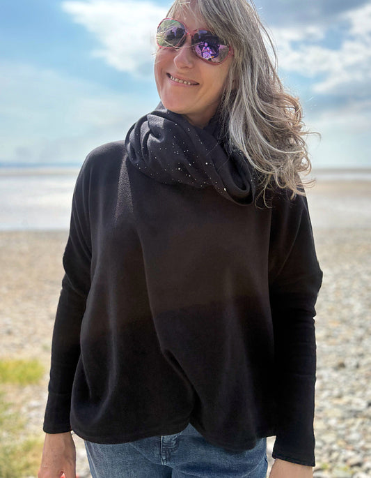 Person wearing a black sweater and snood and sunglasses on a beach