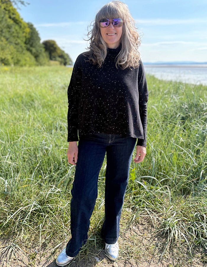Woman standing in a grassy field with a body of water and blue sky in the background