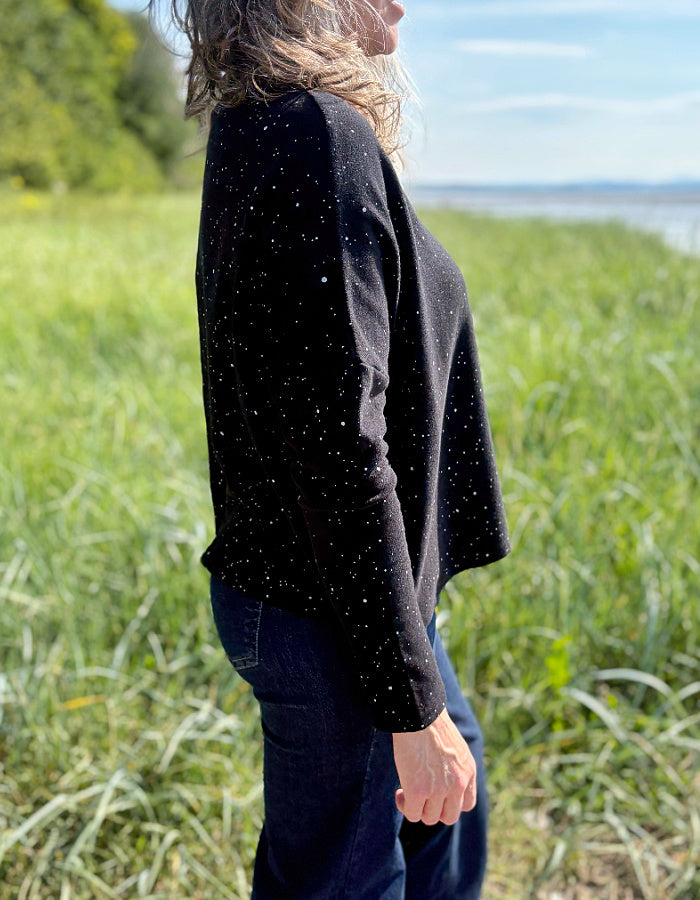 Person wearing a black long-sleeve top standing in a grassy field with a blurred background