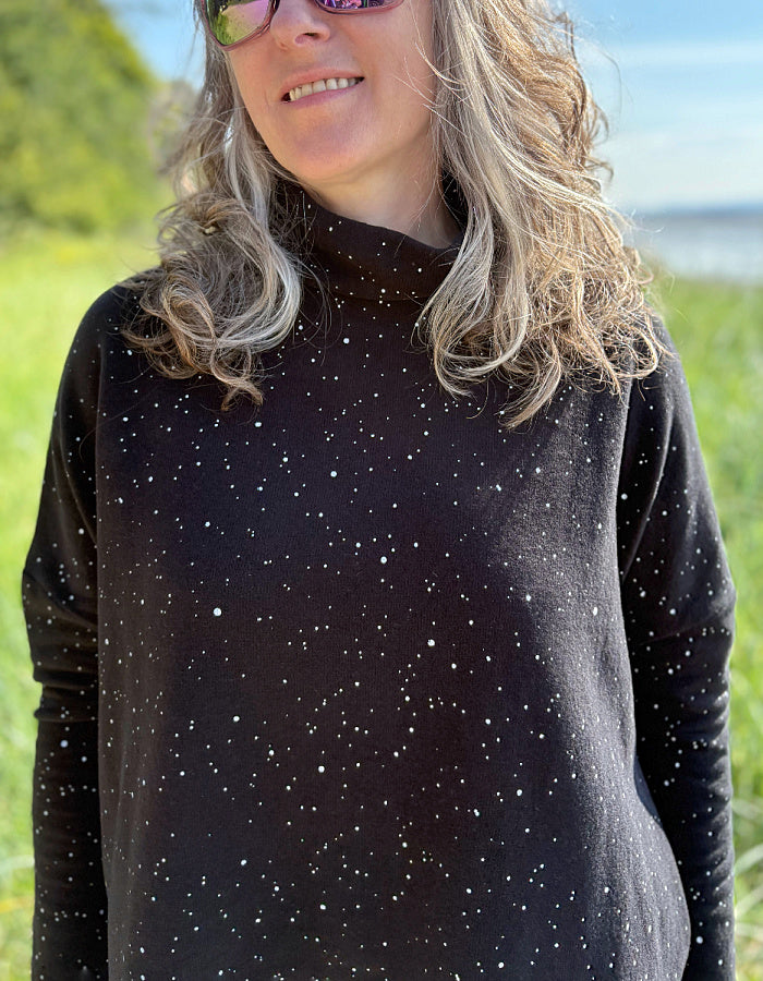 Person wearing a black long-sleeve shirt with white speckles in a grassy field.