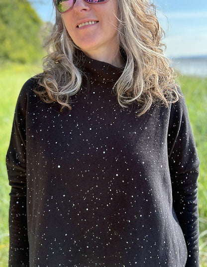 Person wearing a black long-sleeve shirt with white speckles in a grassy field.