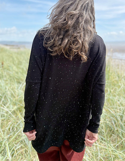 Person standing in a grassy field with a scenic background wearing a black cosy turtle neck tunic and copper brown cord trousers