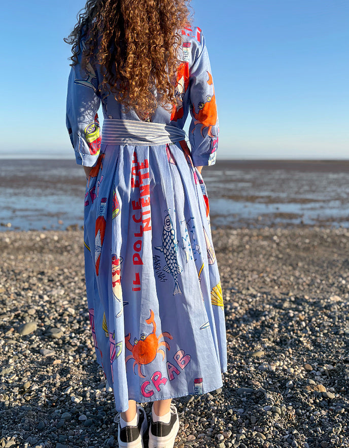 Person wearing a colorful dress with sea-themed designs on a beach.