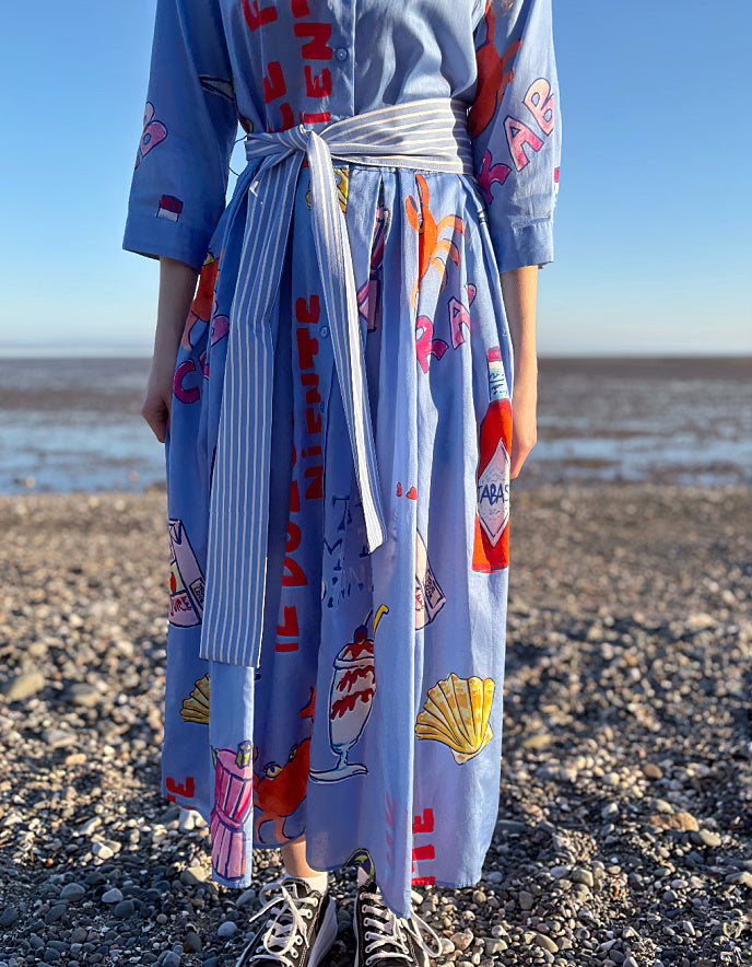 Person wearing a blue dress with colorful graphics on a pebbly beach.
