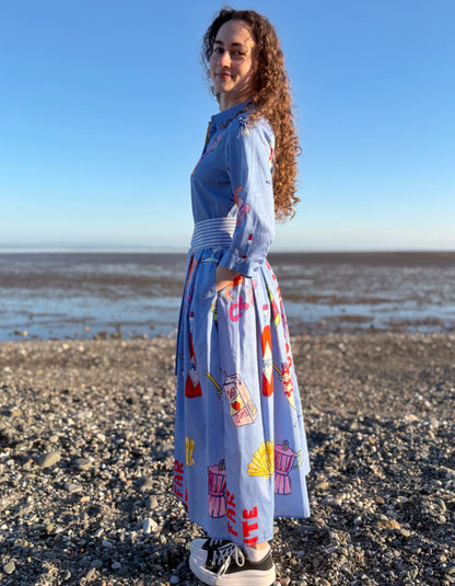 Woman standing on a beach wearing a colorful dress with a pattern of coffee cups and saucers.