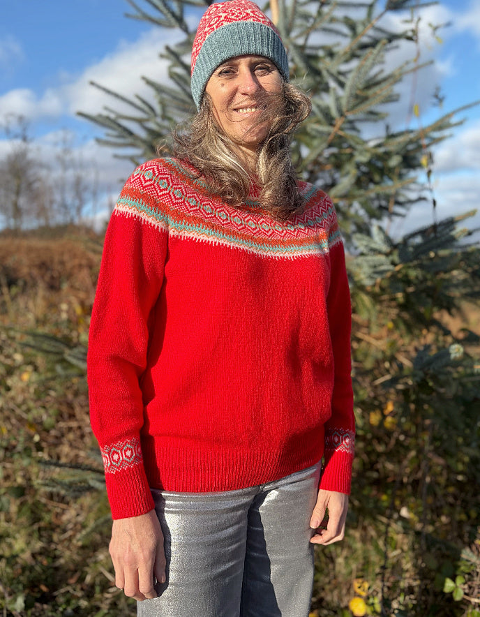 Person wearing a red wool sweater with a patterned fair isle design and a knit hat, standing outdoors.