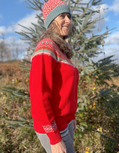 Person wearing a red wool sweater with a patterned fair isle design and a knit hat, standing outdoors.