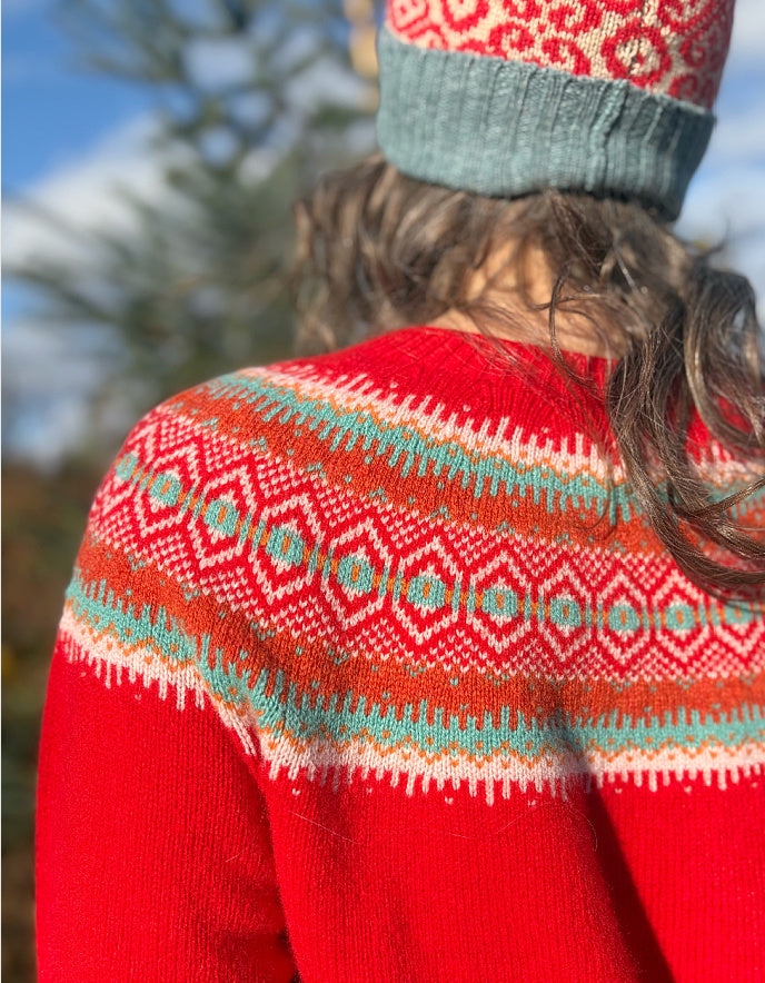 Person wearing a red wool sweater with a patterned fair isle design and a knit hat, standing outdoors.