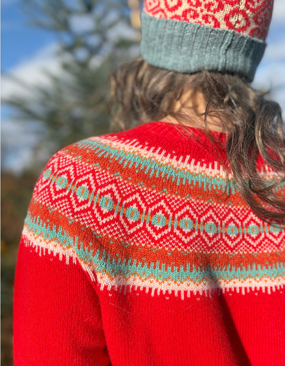 Person wearing a red wool sweater with a patterned fair isle design and a knit hat, standing outdoors.