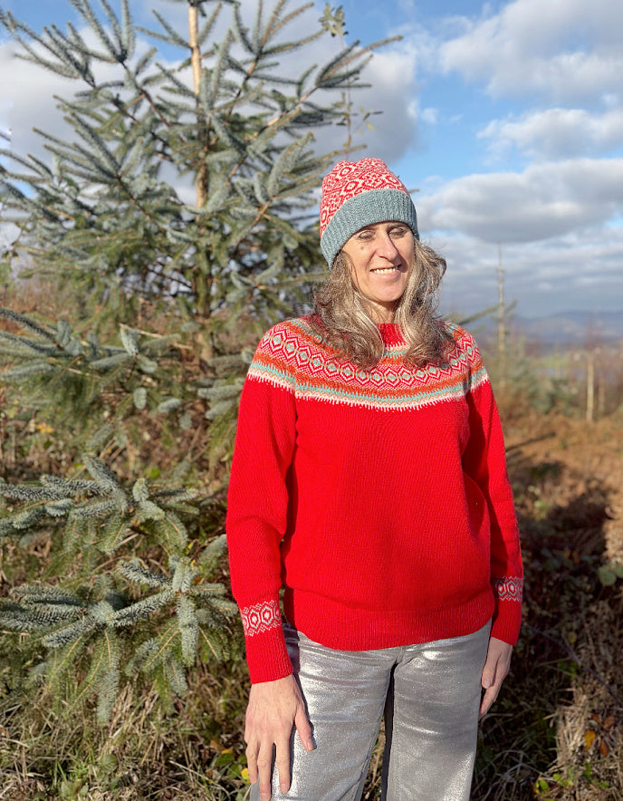 Person wearing a red wool sweater with a patterned fair isle design and a knit hat, standing outdoors.