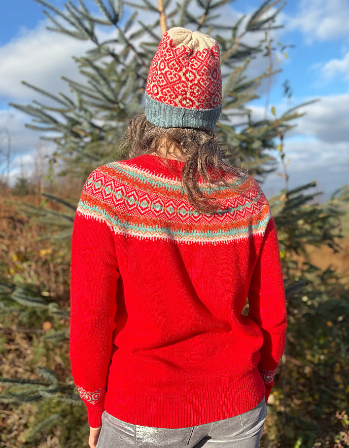 Person wearing a red wool sweater with a patterned fair isle design and a knit hat, standing outdoors.
