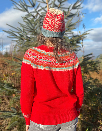 Person wearing a red wool sweater with a patterned fair isle design and a knit hat, standing outdoors.