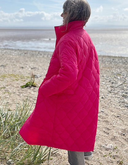 Person wearing a bright pink quilted coat standing on a beach.