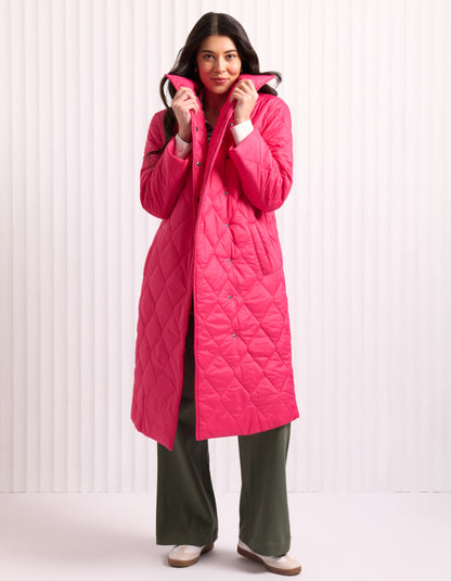 Woman wearing a bright pink midi length puffer coat against a white background