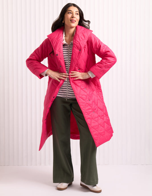 Woman wearing a bright pink midi length puffer coat against a white background