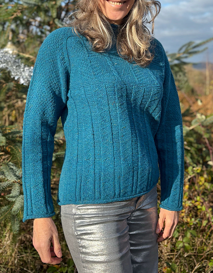 Person wearing a teal blue cable sweater and red beanie outdoors with trees and sky in the background