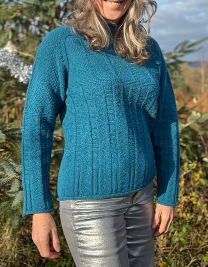 Person wearing a teal blue cable sweater and red beanie outdoors with trees and sky in the background