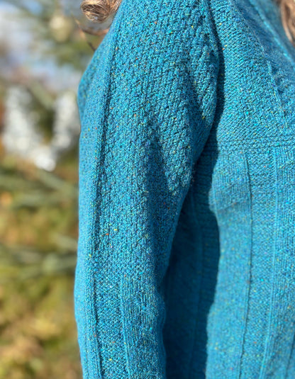 Close-up of a blue knitted donegal tweed sweater sleeve with a blurred natural background