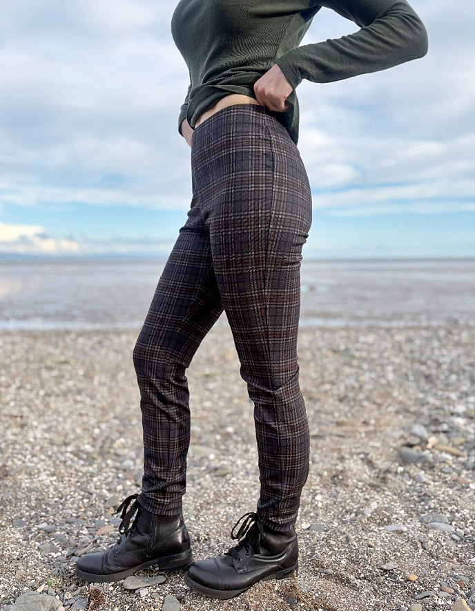 Person wearing grey brown and black plaid print slim fit pull on trousers standing on a beach with ocean and sky in the background