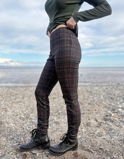 Person wearing grey brown and black plaid print slim fit pull on trousers standing on a beach with ocean and sky in the background