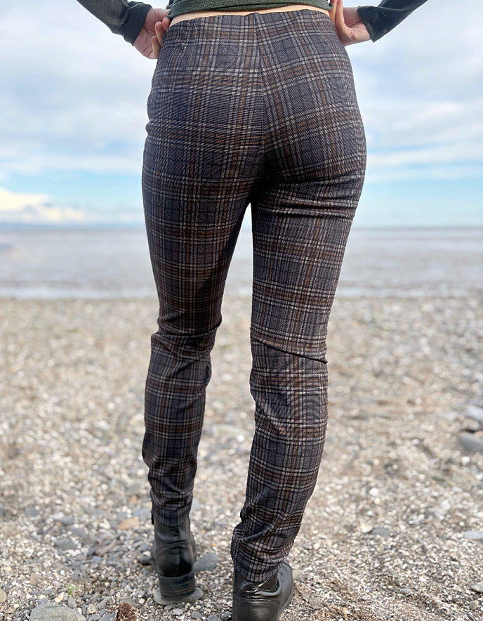 Person wearing grey brown and black plaid print slim fit pull on trousers standing on a beach with ocean and sky in the background