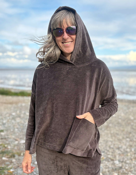 Person wearing a brown cord hooded sweater on a beach with ocean and sky in the background