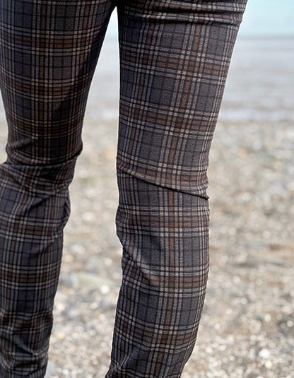 Person wearing grey brown and black plaid print slim fit pull on trousers standing on a beach with ocean and sky in the background