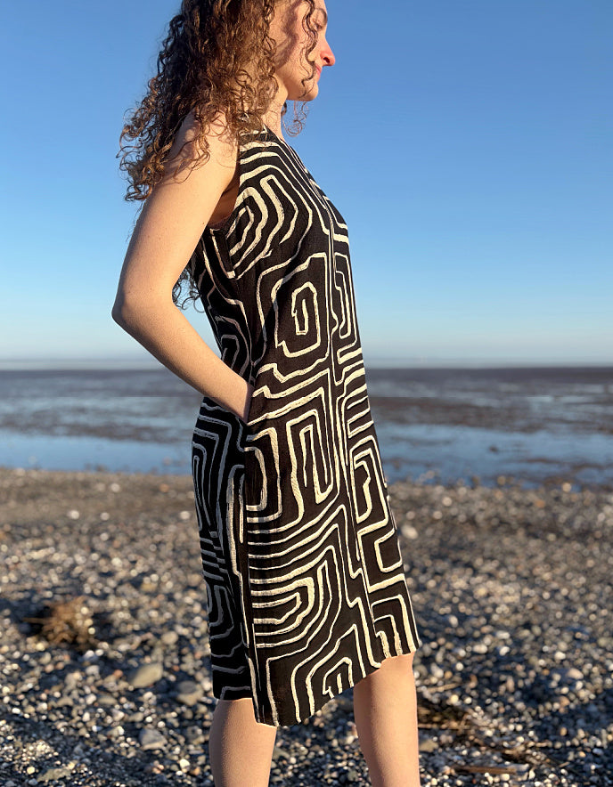 Woman wearing a black and white patterned dress on a pebbly beach with blue sky.